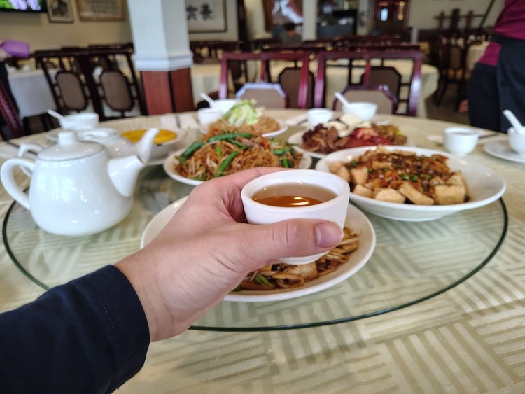 Sun Bo Kong Vancouver | An outstretched hand holding tea with a lazy Susan of food in the background | Homes Almanac