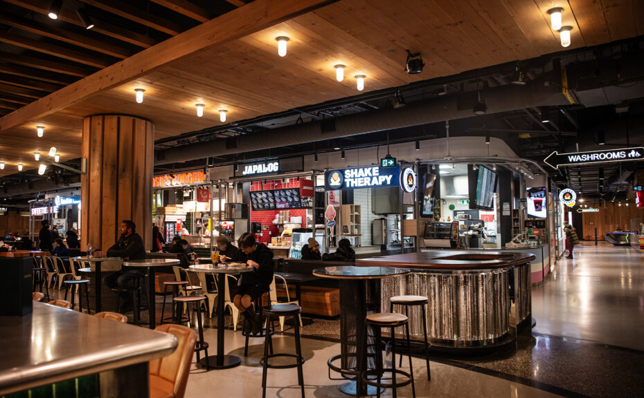 The Well Toronto | Inside The Wellington Market with people sitting at high tables and restaurant kiosks | Homes Almanac