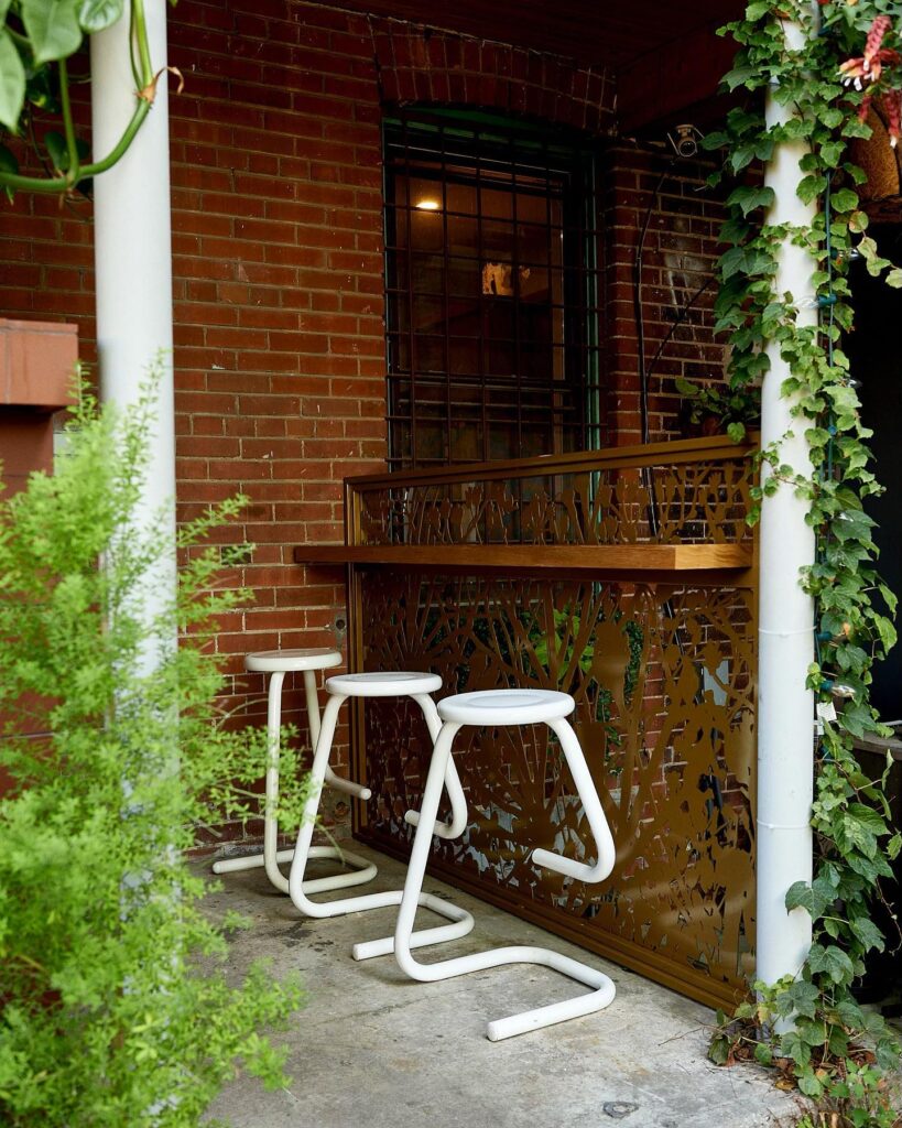 Ossington Wine Crawl | Exterior with red brick wall, lush green plants and bar seating with three bar stools | Homes Almanac