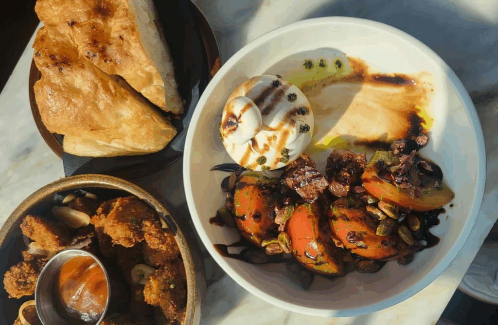 The Rooftop at the Broadview Hotel | Overhead shot of burrata with grilled peaches, chicken bites with sauce and focaccia bread | Homes Almanac