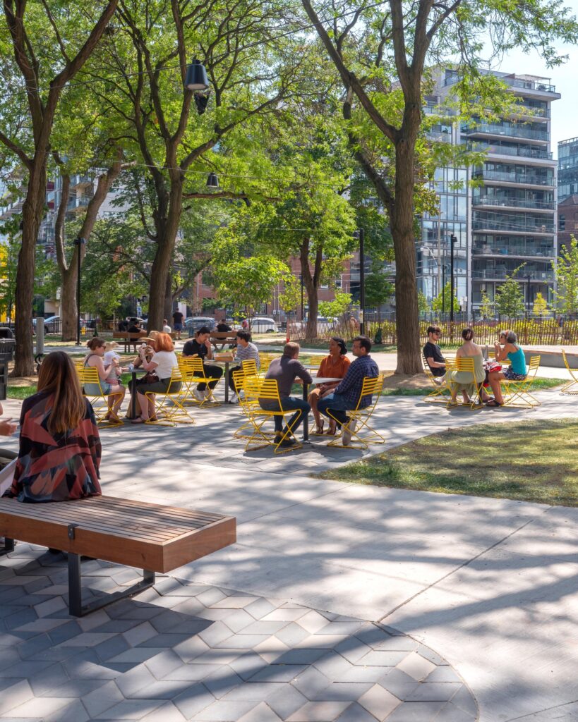 Historic Downtown Toronto Park | People sitting around tables on yellow chairs and benches covered by a treetop canopy on a sunny day | Homes Almanac