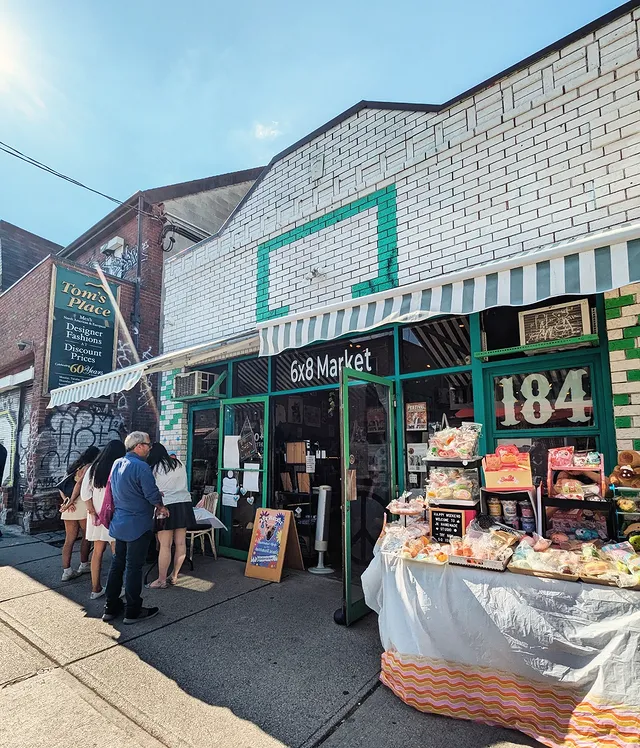 Layers of Kensington Market | Exterior storefront of 6x8 Market with white brick and green and white striped awning with people standing and goods on a table outside | Homes Almanac