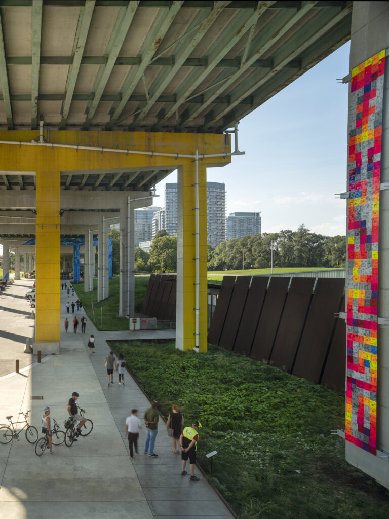 Beneath the Gardiner at The Bentway | A sunny day with people walking and biking through the concrete space, while bright art installations and greenery liven up the space | Homes Almanac