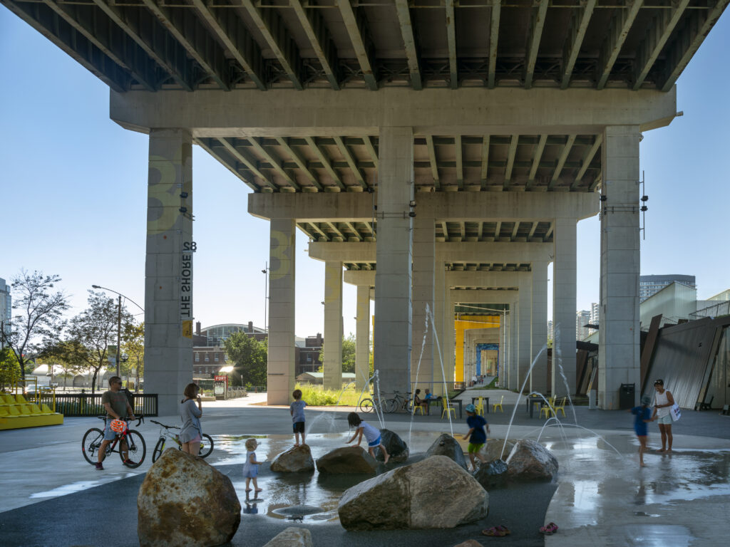 Beneath the Gardiner at The Bentway | Children play in the waterpark installation with oversized rocks | Homes Almanac