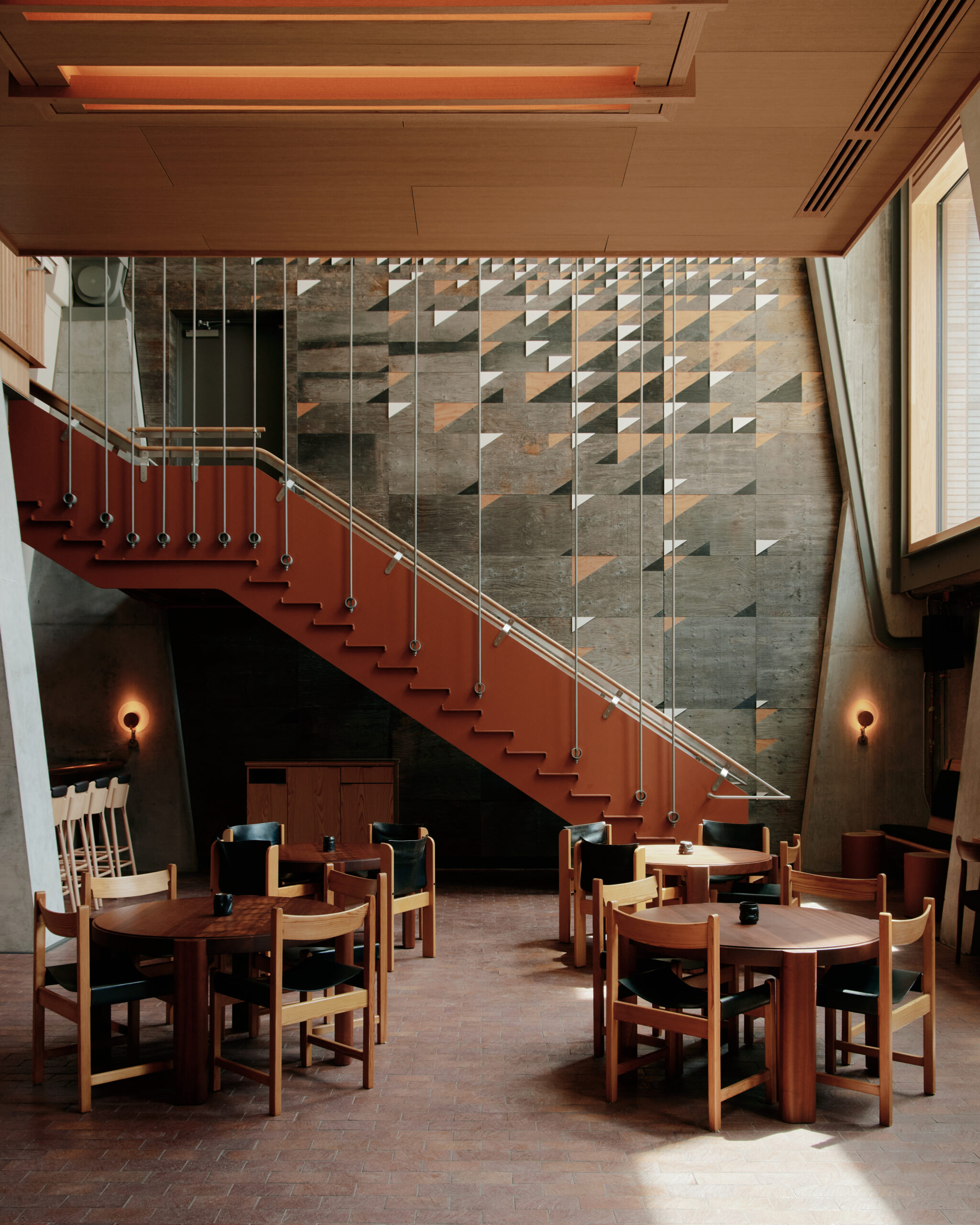Alder | Soft lighting coming from above in a loft style with concrete wall and oak staircase with round tables and chairs | Homes Almanac