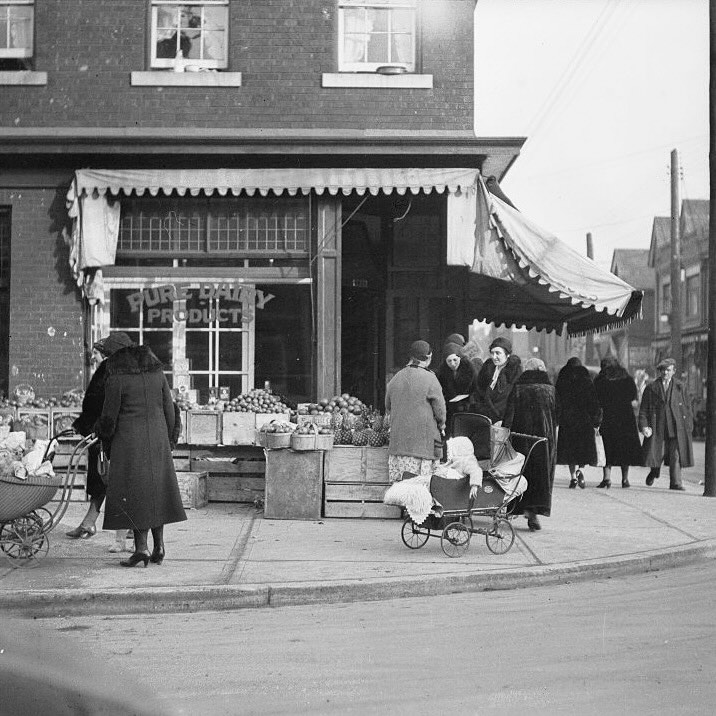 Layers of Kensington Market | Black and white image of Kensington Market 1932 with people walking around a produce market on the corner | Homes Almanac