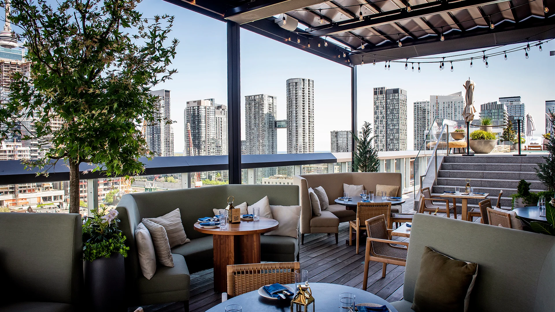 Harriet's Rooftop | Daylight shot of rooftop overlooking Toronto with greenery and green booths with oak round tables and chairs | Homes Almanac