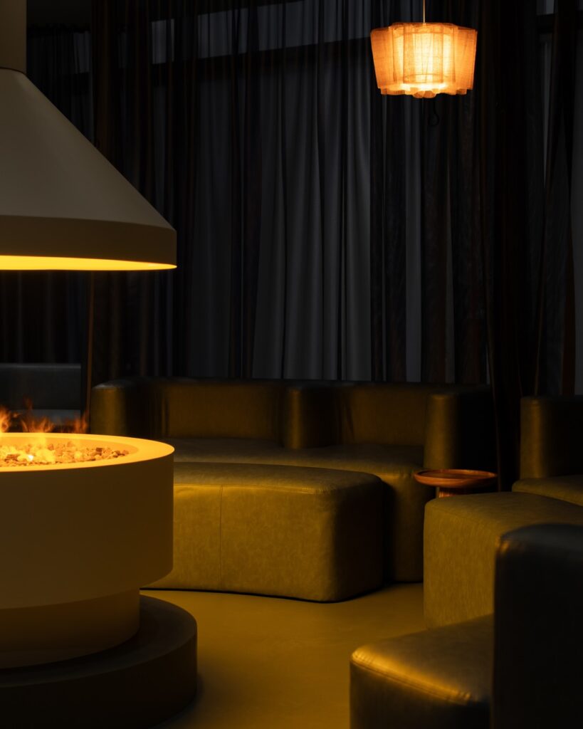 Trove Wellbeing | Dimly lit room with round white fireplace in the center with low, soft green leather seating | Homes Almanac