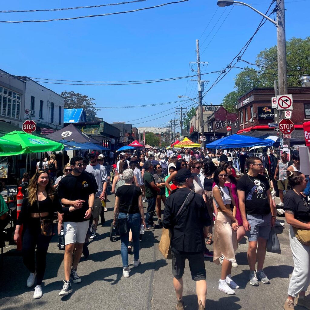 Layers of Kensington Market | A sunny day with people walking through the street, and colourful tents along the sidewalks | Homes Almanac