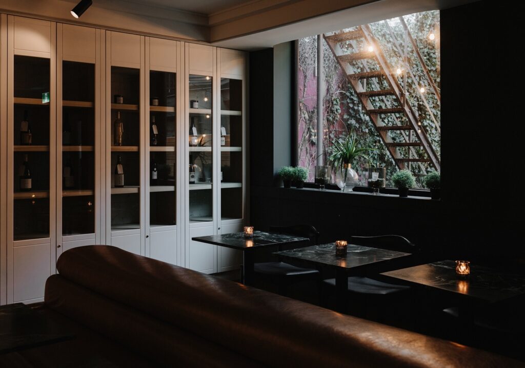 Toronto Hotel Lobbies | Moody shot of The Annex wine bar and lobby with white wine cabinets, and dark seating with black marble tables with a big window in the background | Homes Almanac