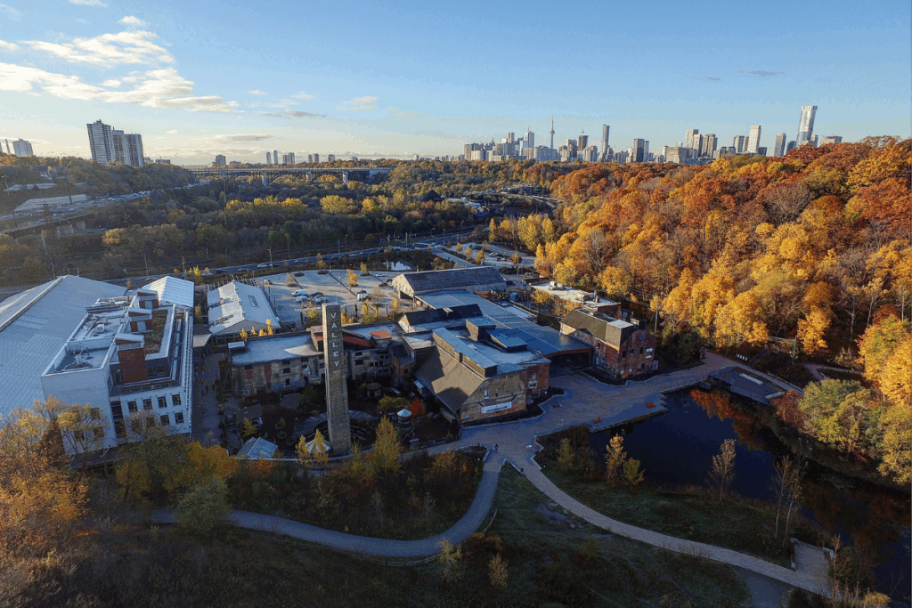 Toronto Farmers Markets | Aerial shot of Evergreen Brickworks in Fall with orange and yellow trees and a view of downtown Toronto | Homes Almanac