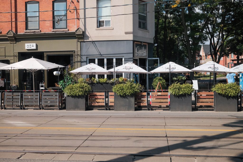 history of trinity bellwoods and ossington | Bright sunny day with white sun umbrellas out and outdoor seating | Homes Almanac