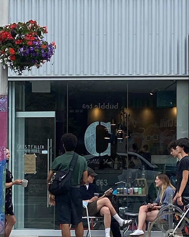 Crestfallen | Exterior with shipping container style white and floor to ceiling windows with a "C" painted on and people sitting outside and chatting | Homes Almanac