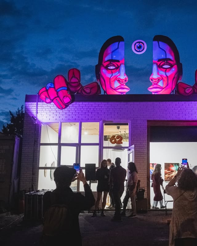 Geary Ave | A night shot of an art installation on the roof of a building of a woman's face and hands split into two illuminated in pinks purples and blue with a third eye in the middle | Homes Almanac