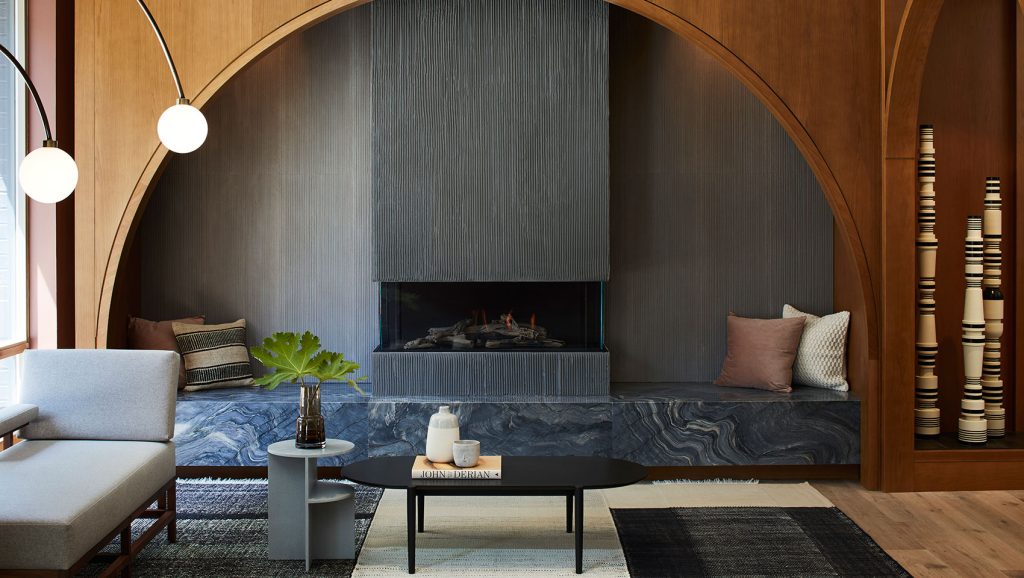 Kimpton Saint George | A grey textured gas fireplace sitting on a deep blue marble bench under a cedar wood arch | Homes Almanac