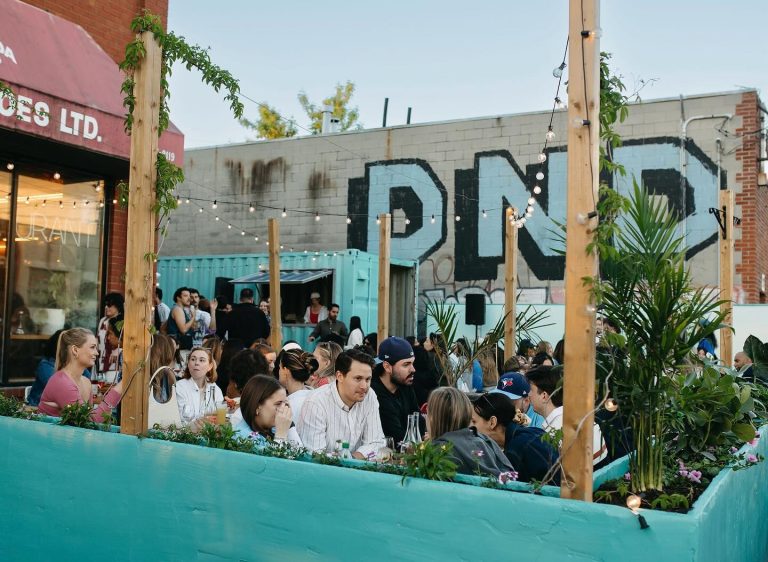Geary Ave | Warm evening with people sitting outside on a patio with turquoise painted barriers | Homes Almanac