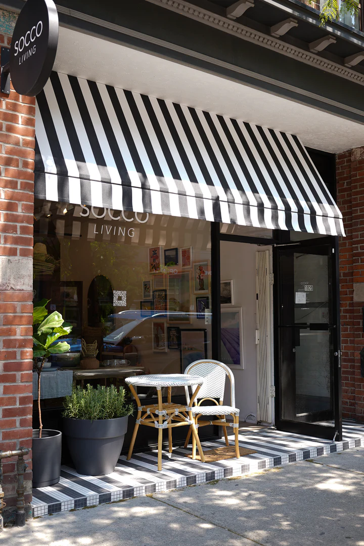 SOCCO Living | Sunny day with a black and white striped awning over floor to ceiling glass window sand a barista set in front of the shop | Homes Almanac