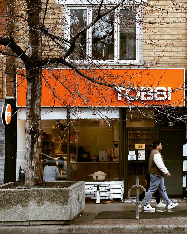 Tobbi Cafe | An orange sign with "Tobbi" written in white with a man walking past and a bare tree on the left | Homes Almanac