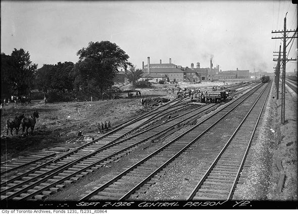 History of Liberty Village | Central prison yard in 1926 liberty village with workers and railway tracks on black and white | Homes Almanac