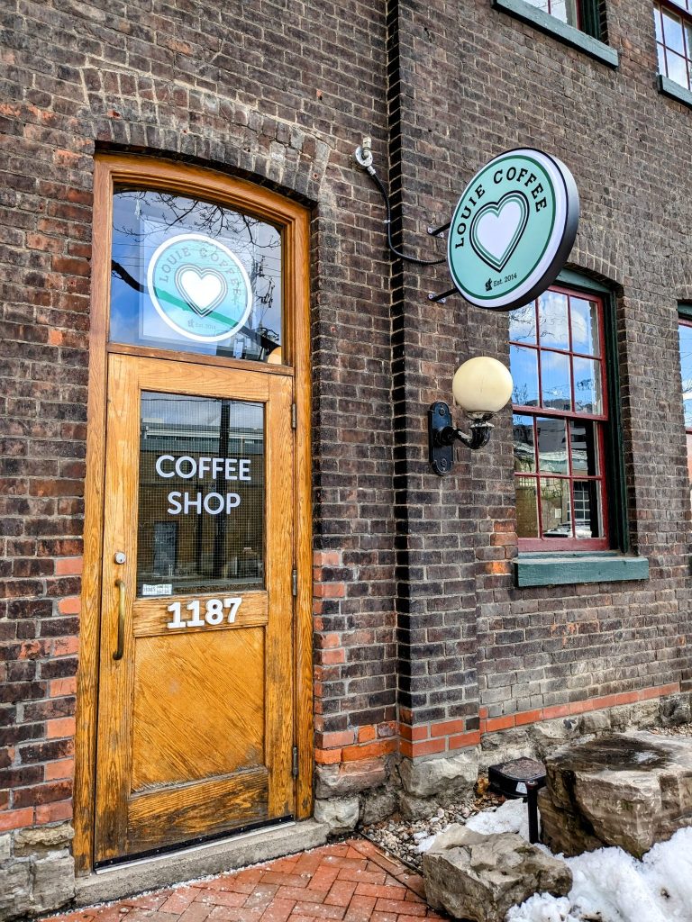 Louie Coffee | Brick exterior with a quaint wooden door and a circle sign above the door | Homes Almanac