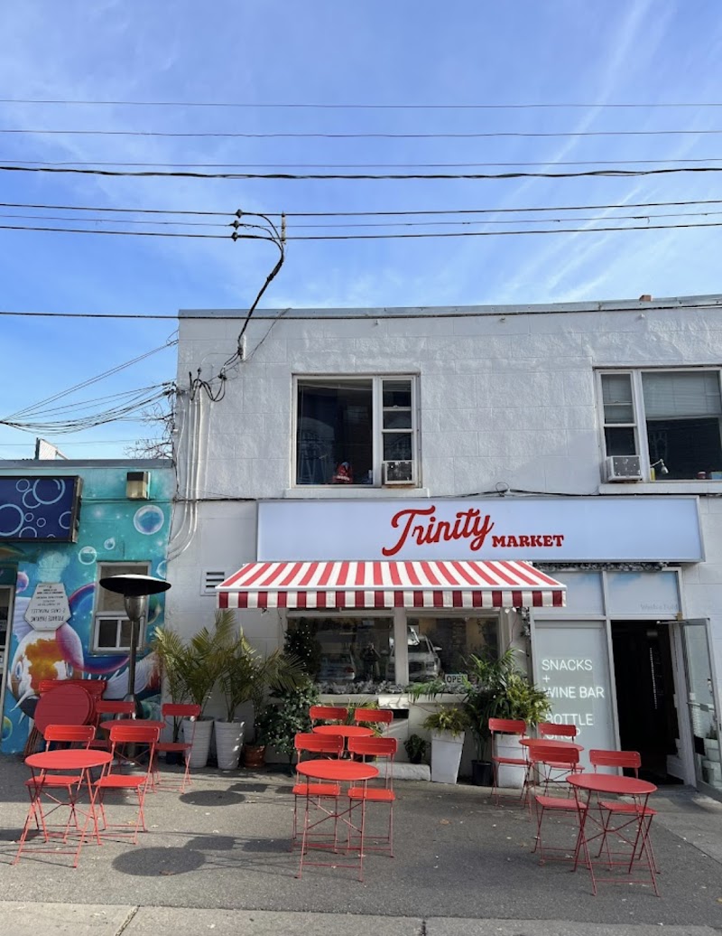 Trinity Market | Sunny day with a white building and red and white awning with red outdoor seating | Homes Almanac