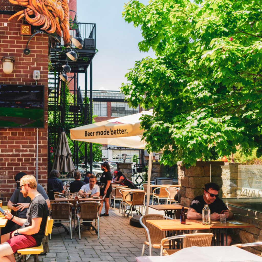 Brazen Head Irish Pub | A patio on a sunny day with people sitting at tables, a tree and yellow sun umbrella | Homes Almanac