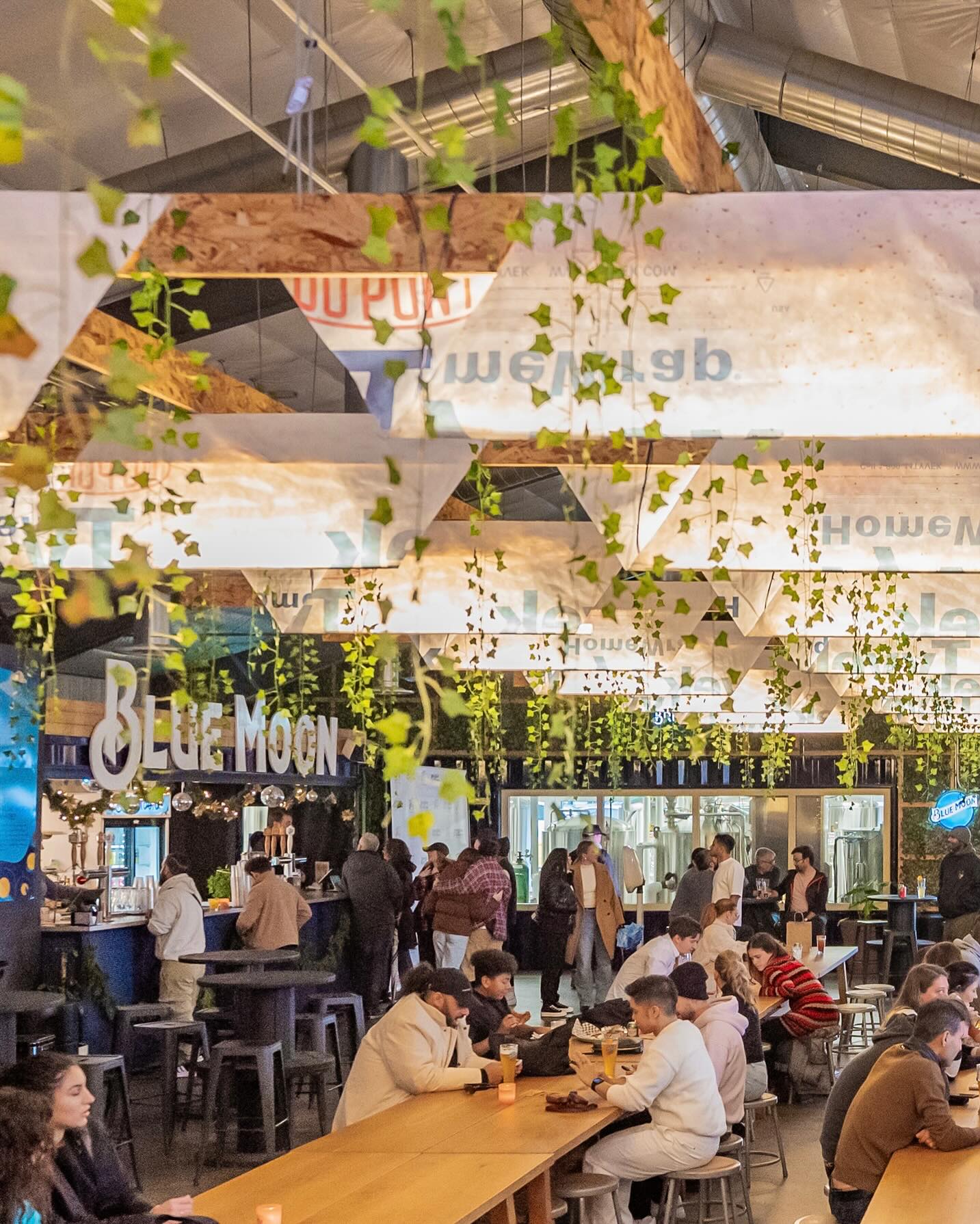 clubhouse @ stackt market | Afternoon shot of a full event space with people sitting at long benches and greenery hanging from the ceiling | Homes Almanac