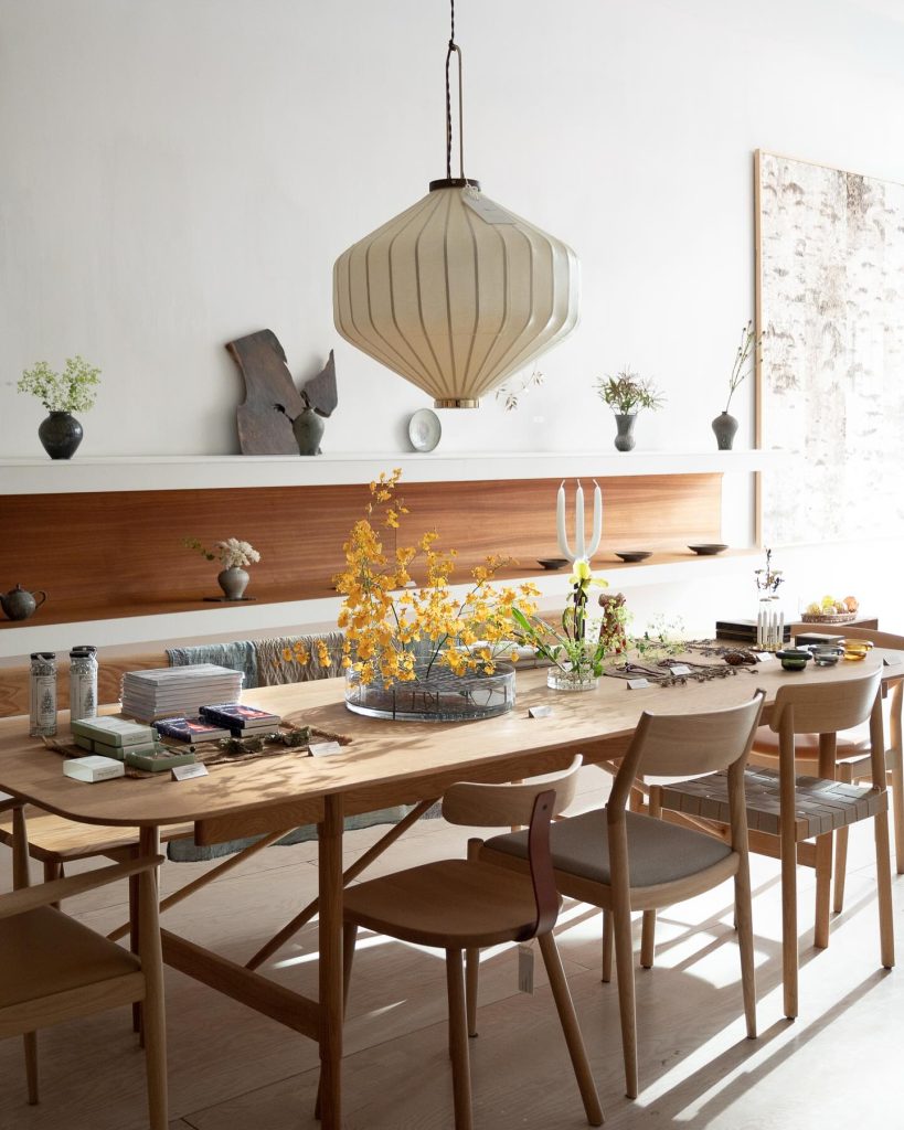 Mjolk | Bright naturally lit room with light oak dining table and chairs and a paper hanging lamp with minimal table decor | Homes Almanac