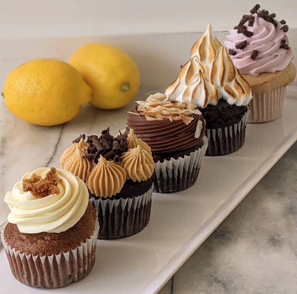 Vancouver gluten-free bakery | Four cupcakes lined up on a marble counter of various toppings and flavours with 2 lemons sitting behind them | Homes Almanac
