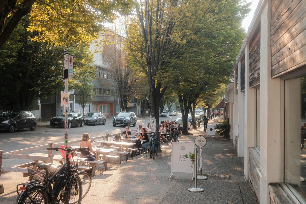Vancouver Conscious Consumer Culture | Soft daylit and treelined street with people sitting outside on a patio | Homes Almanac